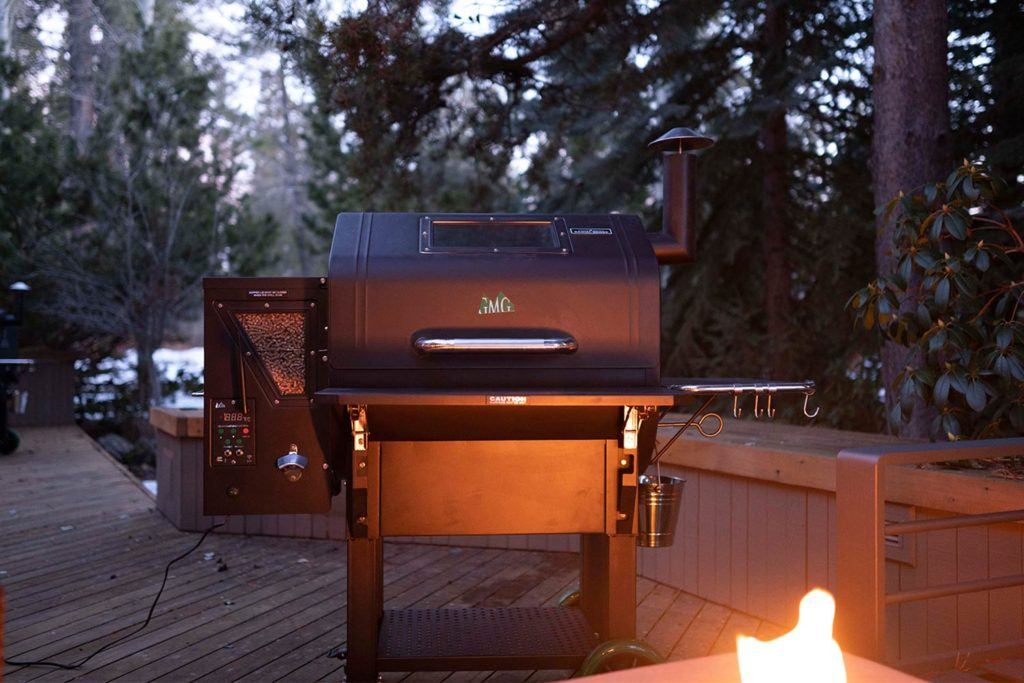 a smoker BBQ with wood pellet attachment on a backyard patio at dusk